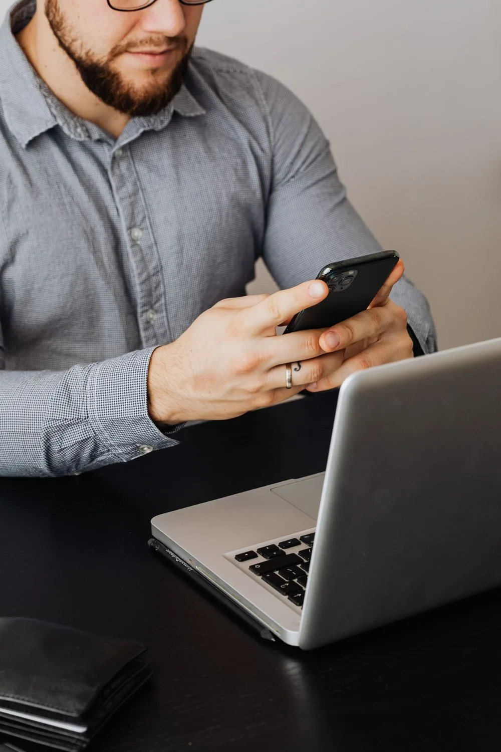 Dono de negócio respondendo mensagens no celular enquanto trabalha no notebook