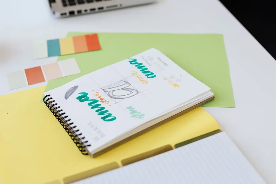 Caderno com rascunhos de logotipo à mão e amostras de cores sobre uma mesa branca