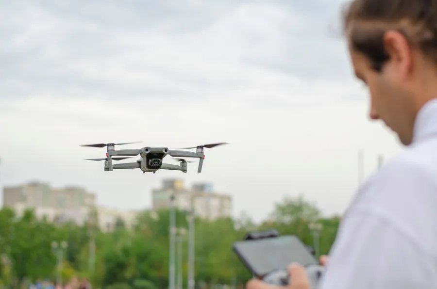 Operador pilotando um drone que sobrevoa árvores e prédios