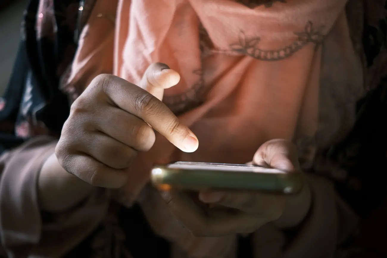 Close de uma mão tocando a tela de um celular no escuro