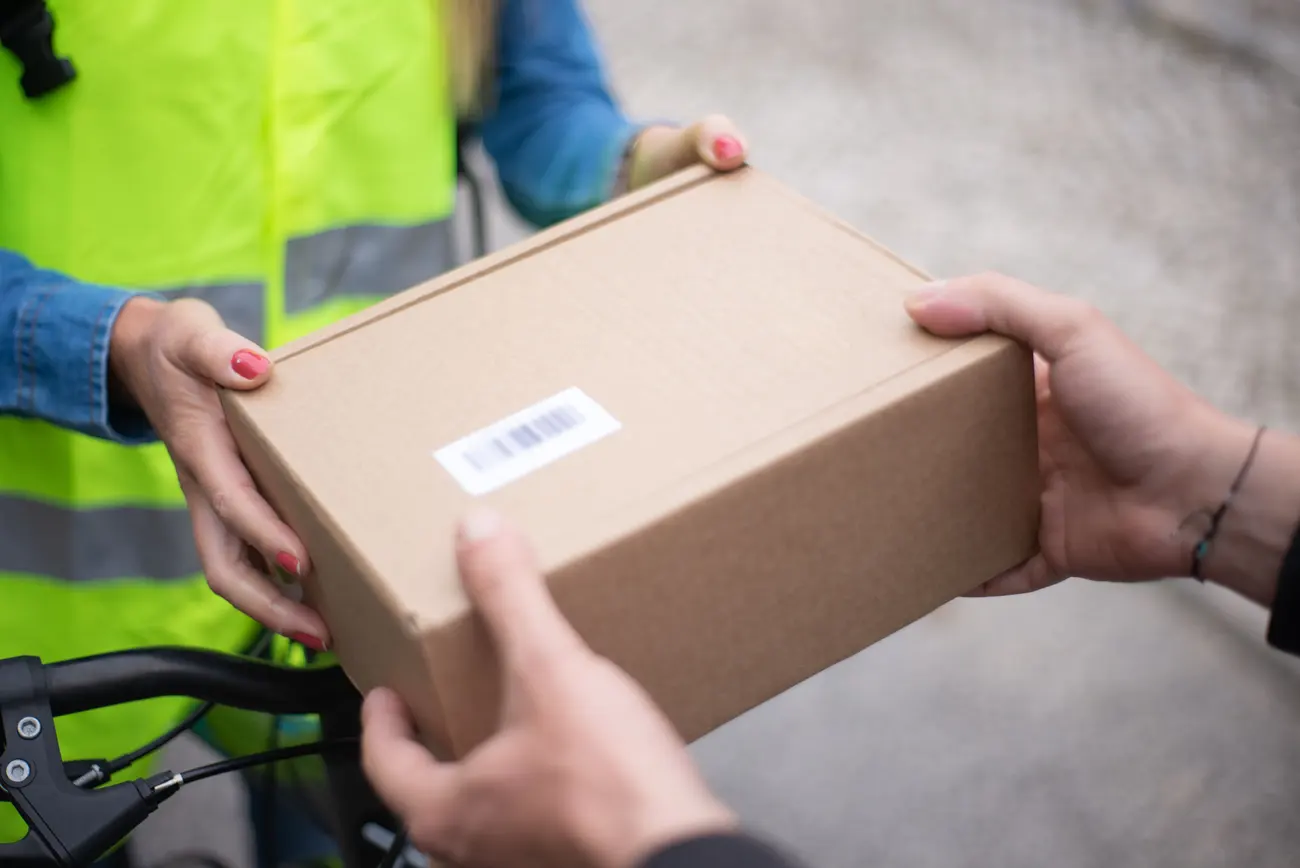 Entregador de bicicleta passando uma caixa com etiqueta de rastreio para o cliente