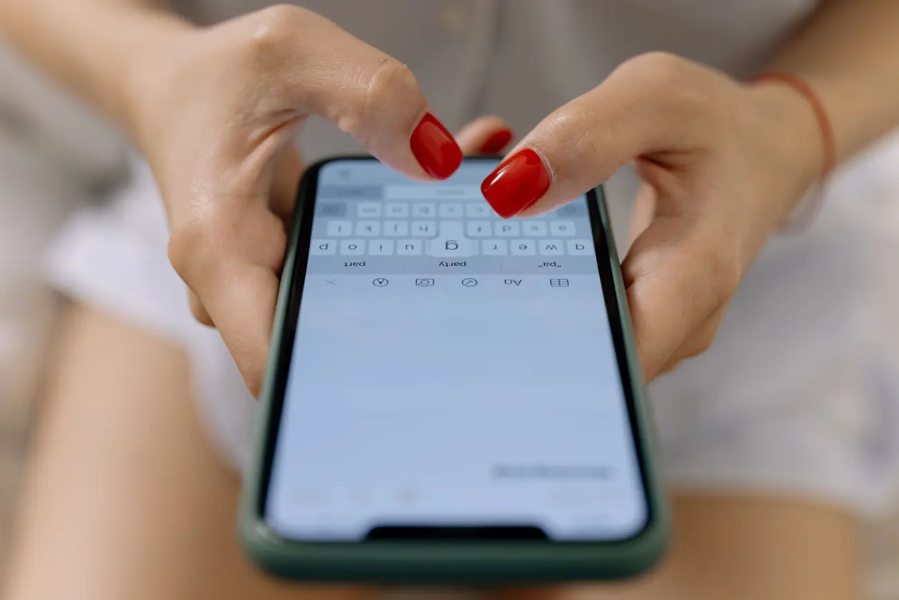 Mãos com unhas vermelhas digitando no teclado do celular durante uma conversa