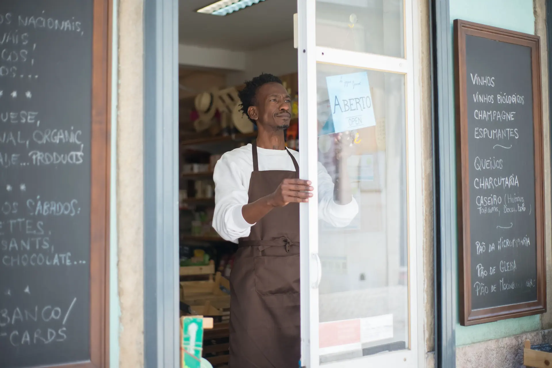 Dono de loja abrindo a porta com a placa Aberto, esperando o primeiro cliente do dia