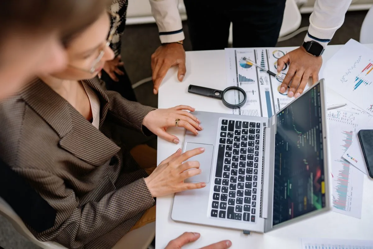 Equipe reunida em volta de um notebook analisando gráficos de desempenho impressos e na tela