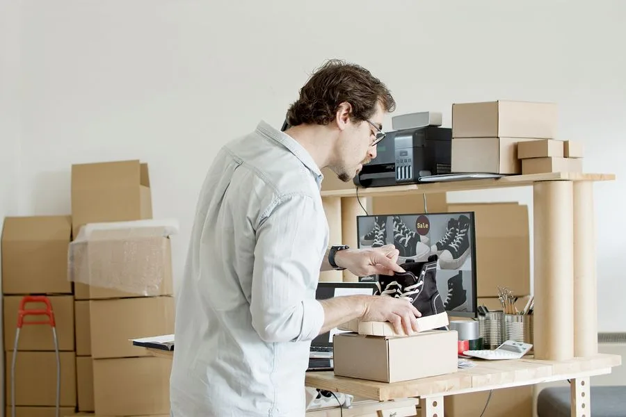 Dono de loja virtual embalando um par de tênis em caixa de papelão para envio