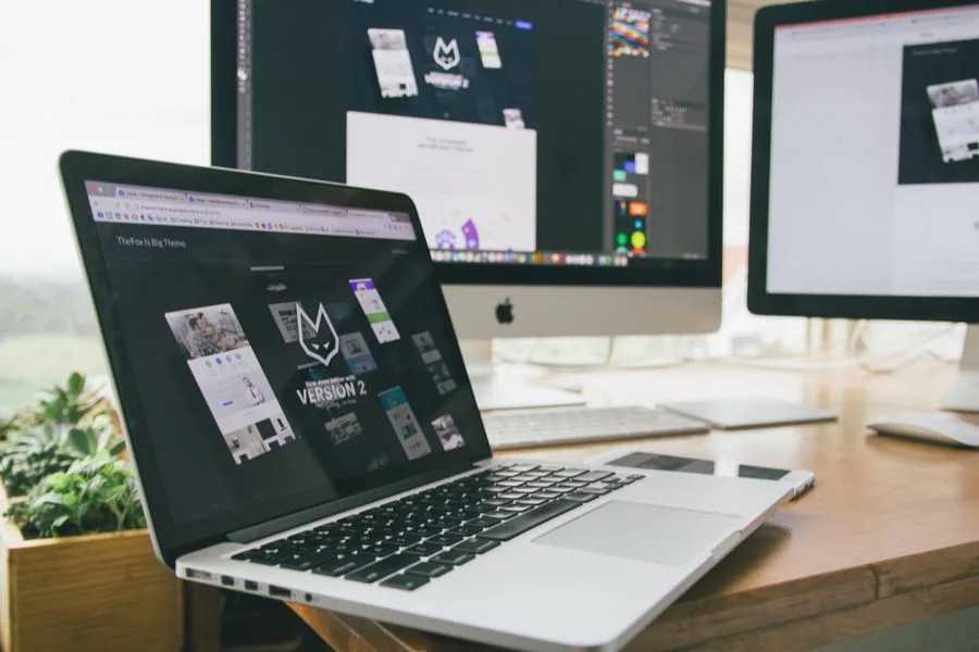 Mesa de trabalho com notebook e monitores mostrando um software de design de sites