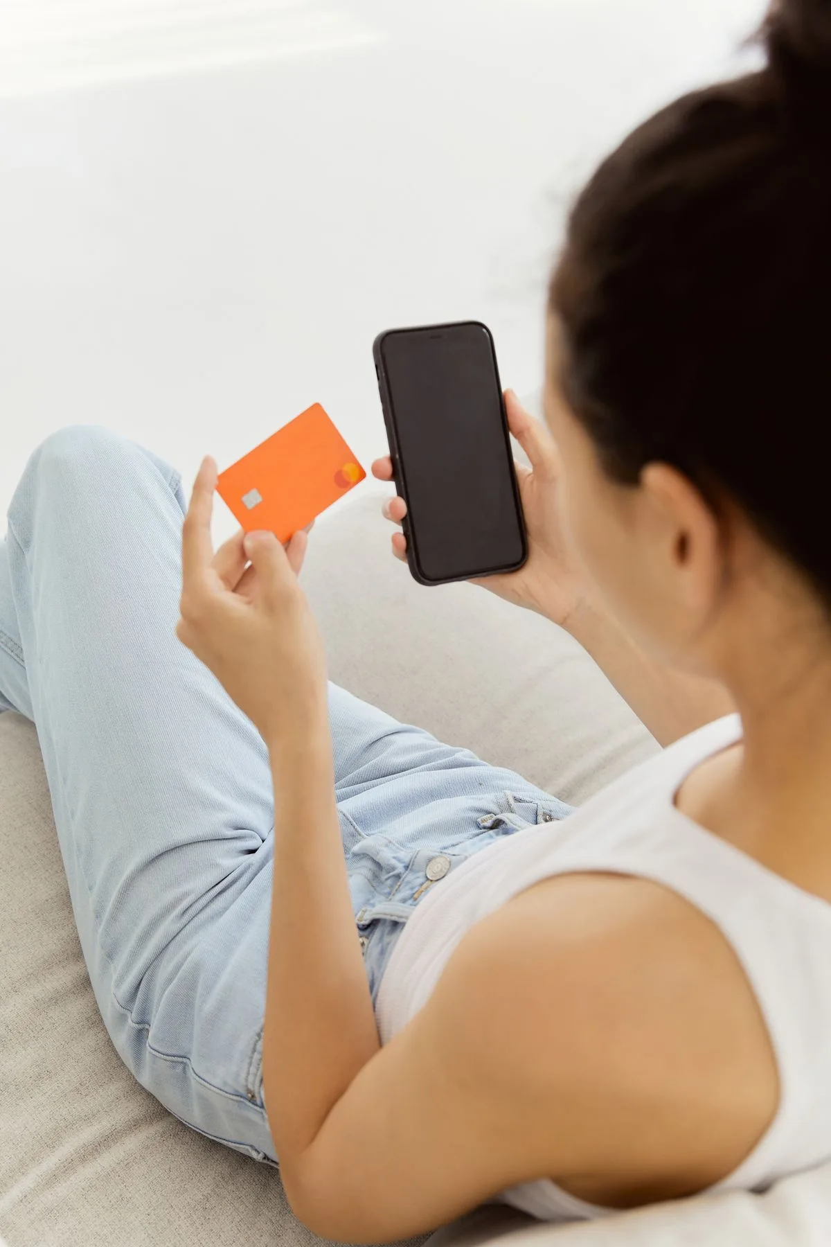 Cliente no sofá de casa comprando pelo celular com o cartão na mão