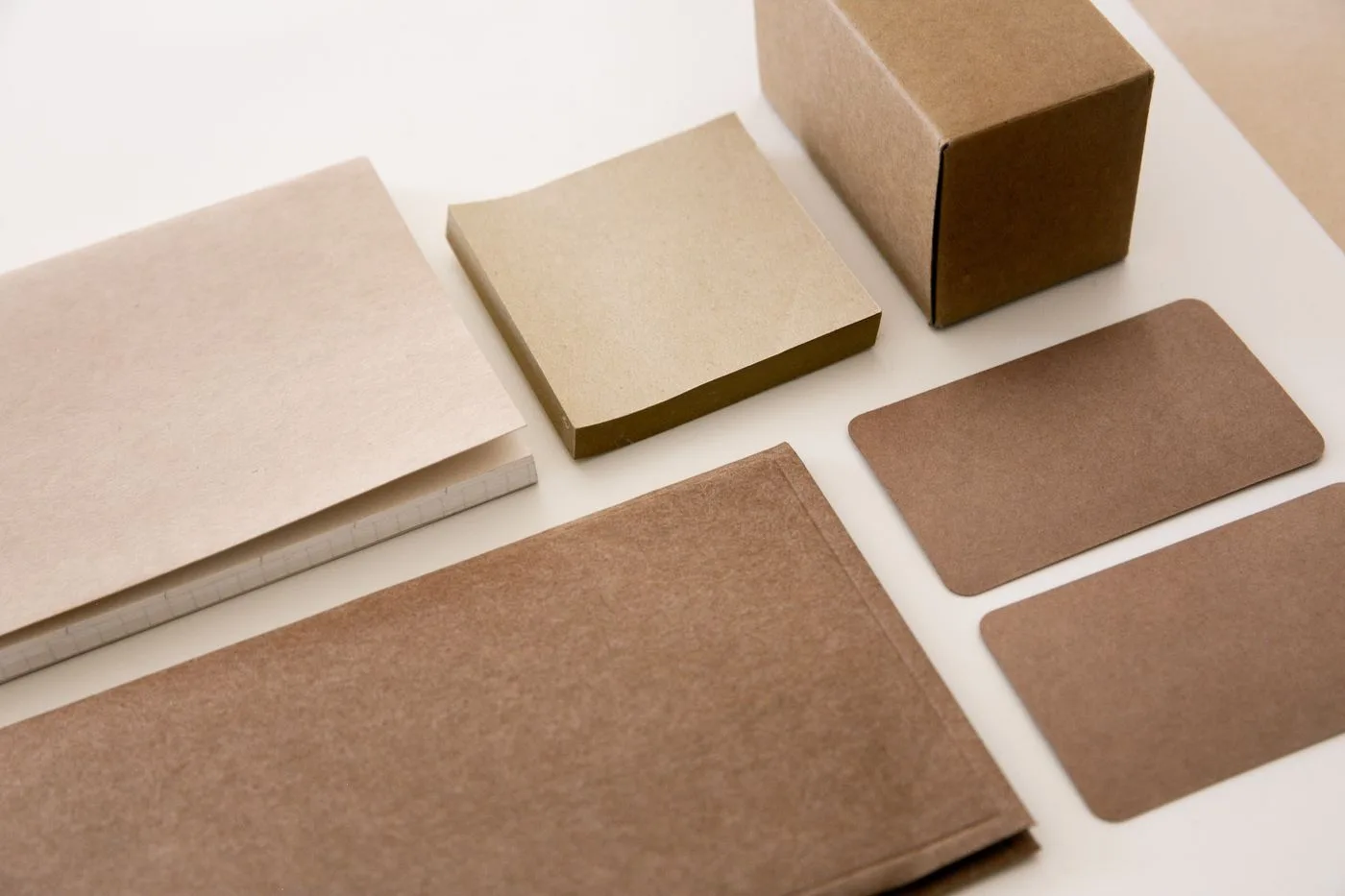 Conjunto de papelaria em papel kraft alinhado sobre a mesa: envelope, bloco, caixa e cartões de visita
