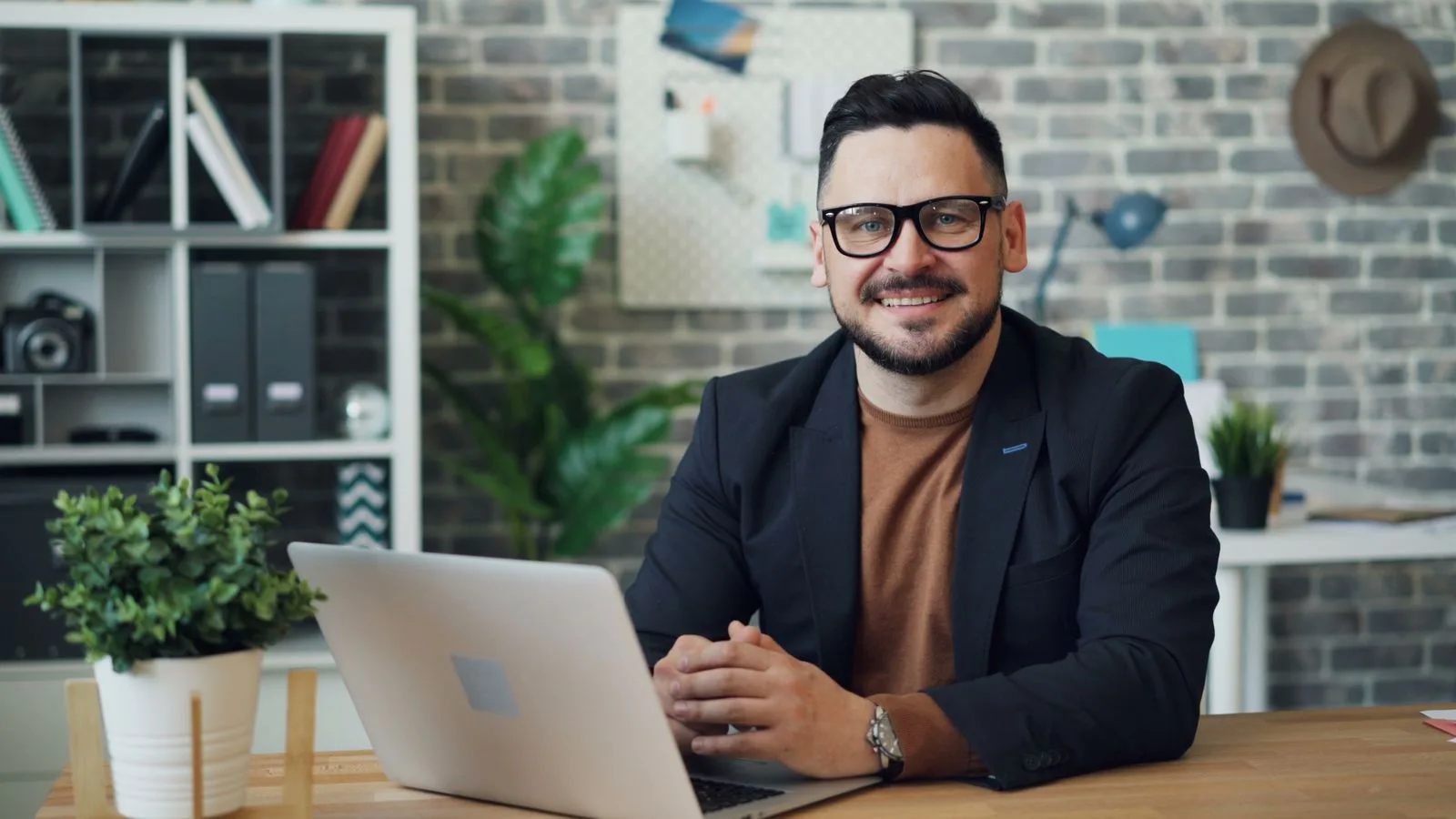 Dono de empresa sorrindo com o notebook aberto na mesa do escritório