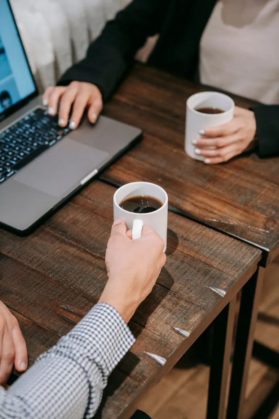 Duas pessoas conversando sobre um negócio numa mesa de madeira, com notebook e café